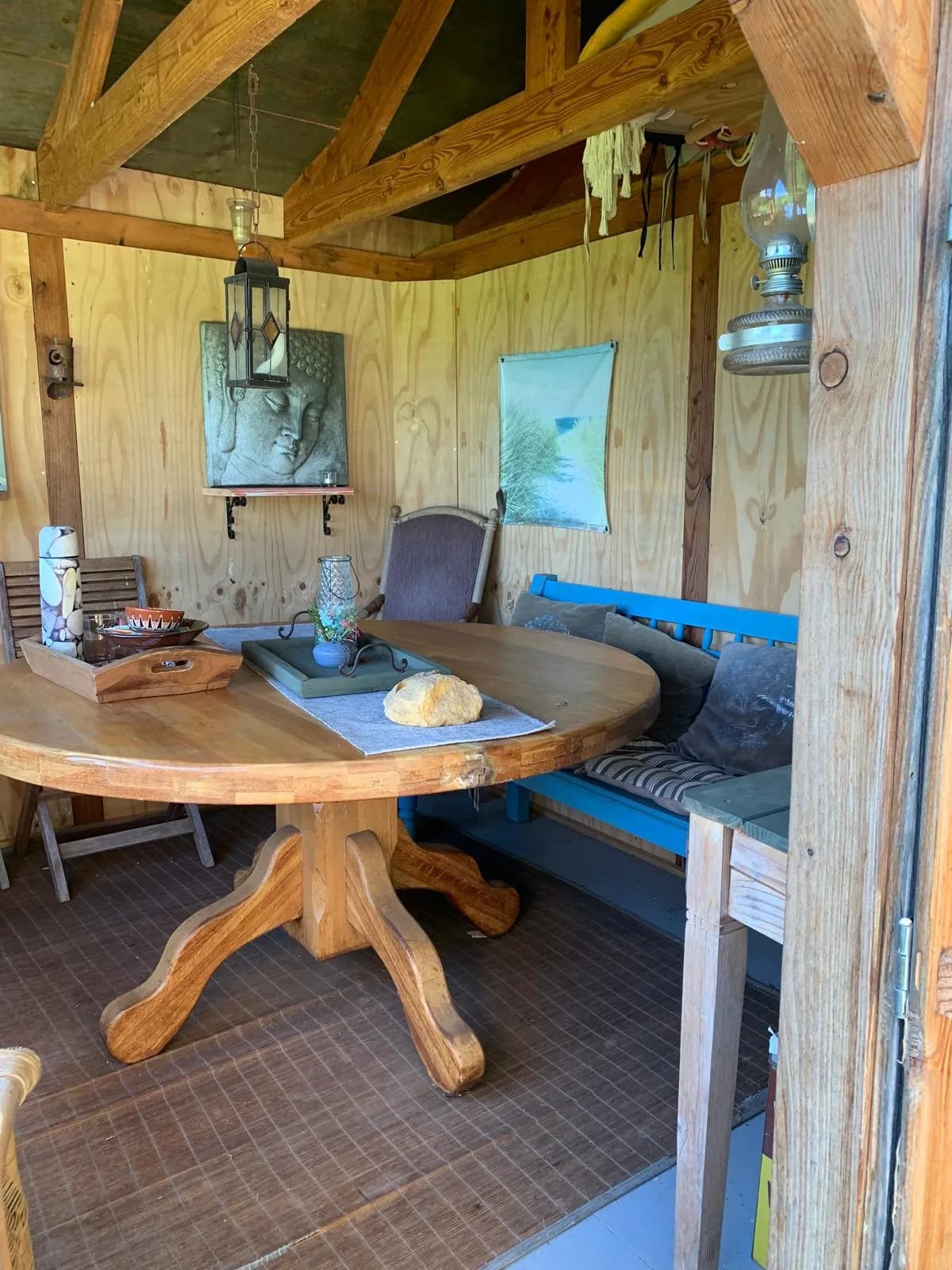 Beschutte houten buitenruimte met een ronde tafel en een blauwe bank